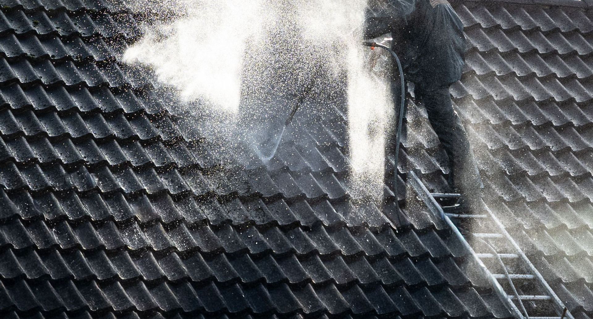 Worker power washing roof tiles, removing grime and buildup.